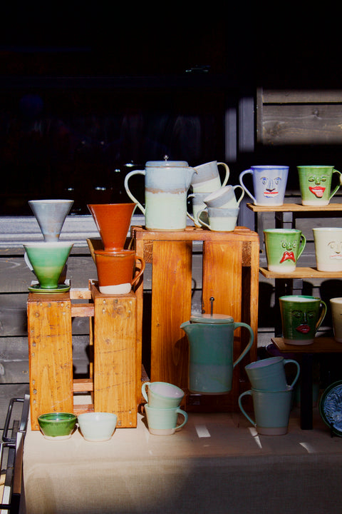 Collection of colorful ceramic mugs and bowls on wooden stands against a dark background