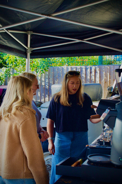 Woman in a blue shirt and sunglasses teaching latteart to customers