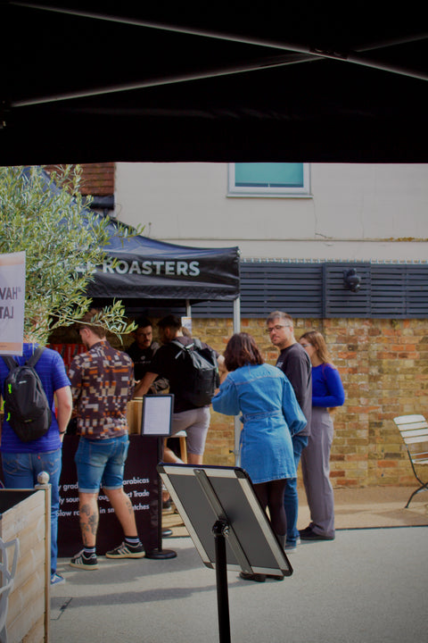 People gathered around a booth with 'Roasters' branding in an outdoor setting.