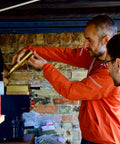 Two people working with a coffee roasting machine against a brick wall.