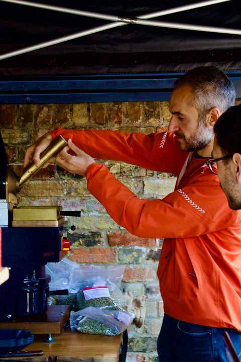Two people working with a coffee roasting machine against a brick wall.