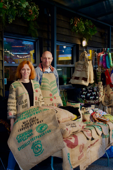 Two people standing behind a table with reusable bags in front of a store entrance.